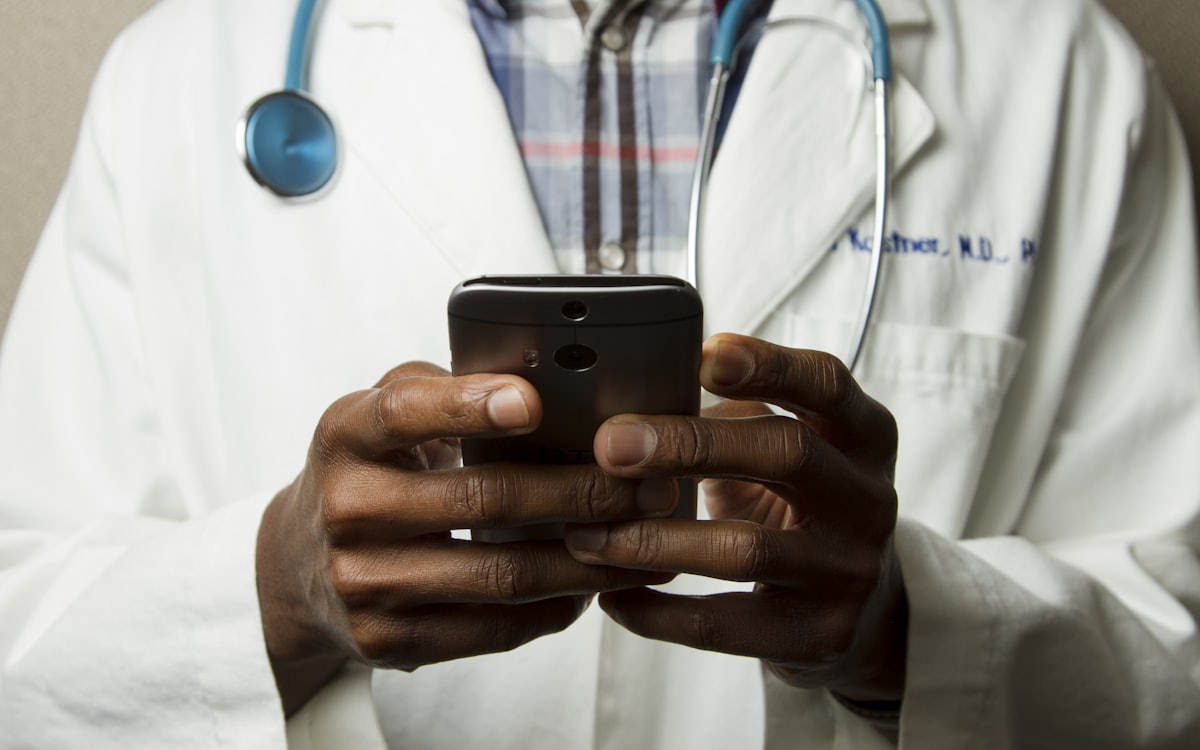 Clinician using a mobile phone while wearing a white coat and stethoscope
